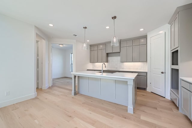 kitchen featuring sink, light hardwood / wood-style flooring, gray cabinetry, and an island with sink