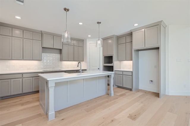 kitchen featuring sink, light hardwood / wood-style flooring, a kitchen island with sink, and gray cabinetry