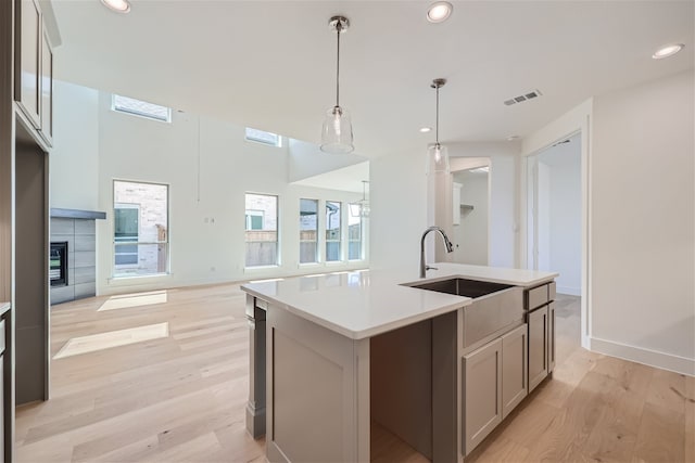 kitchen featuring gray cabinets, pendant lighting, a center island with sink, sink, and light hardwood / wood-style flooring