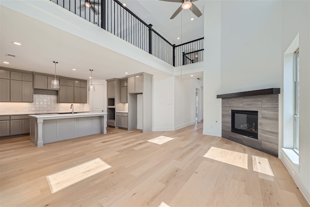 kitchen featuring a high ceiling, light hardwood / wood-style floors, gray cabinets, a kitchen island with sink, and a tiled fireplace