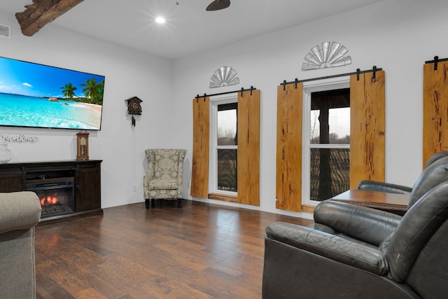 living room featuring a barn door, ceiling fan, beamed ceiling, and dark wood-type flooring