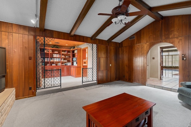 living room featuring lofted ceiling with beams, wooden walls, ceiling fan, and light carpet