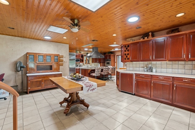 kitchen with light tile floors, a skylight, ceiling fan, tasteful backsplash, and island exhaust hood