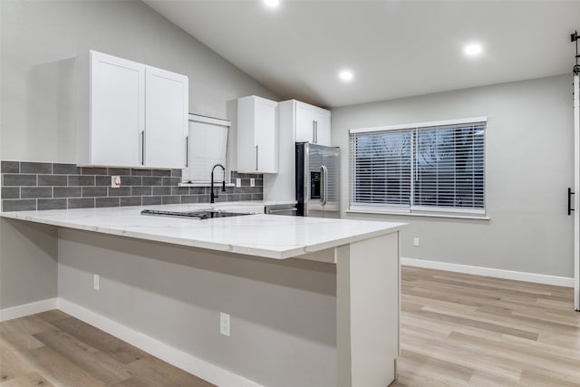 kitchen with white cabinets, stainless steel refrigerator with ice dispenser, light wood-type flooring, and kitchen peninsula