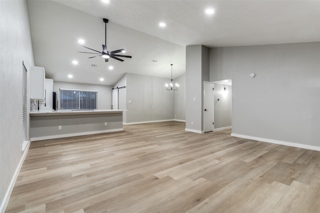 unfurnished living room with a barn door, light hardwood / wood-style floors, and high vaulted ceiling