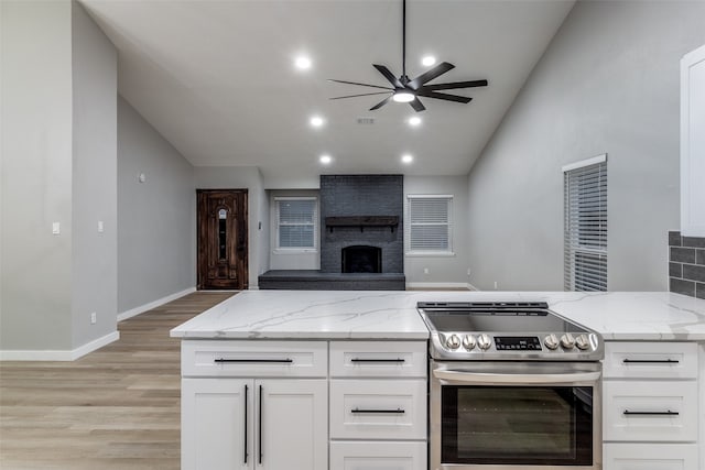 kitchen with stainless steel range with electric cooktop, light stone countertops, a fireplace, and white cabinetry