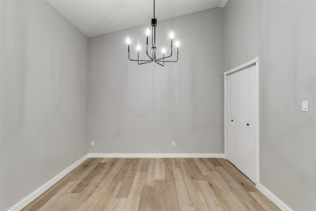 unfurnished dining area featuring light hardwood / wood-style flooring, lofted ceiling, and a notable chandelier