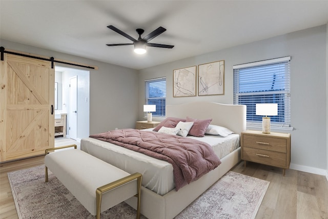 bedroom with a barn door, ceiling fan, light hardwood / wood-style flooring, and ensuite bathroom