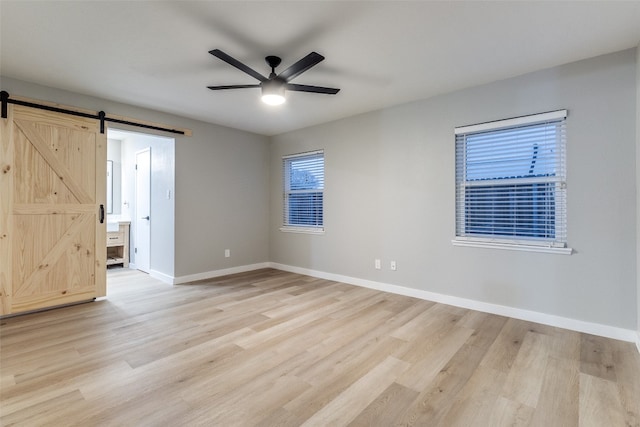 empty room featuring light hardwood / wood-style floors, ceiling fan, and a barn door