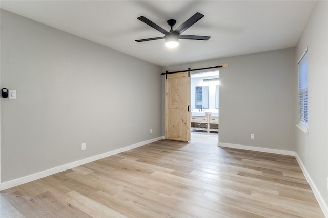 spare room featuring light hardwood / wood-style floors, ceiling fan, and a barn door