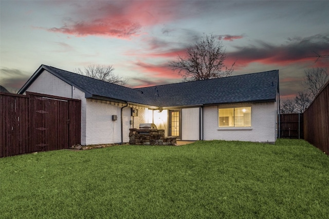 back house at dusk featuring a lawn