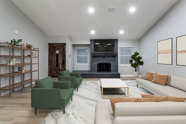 living room with light wood-type flooring, vaulted ceiling, and a large fireplace