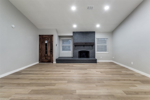 unfurnished living room featuring a brick fireplace and light hardwood / wood-style floors