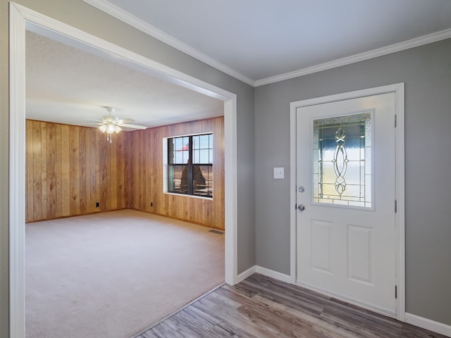 carpeted entrance foyer with wooden walls, ceiling fan, and crown molding