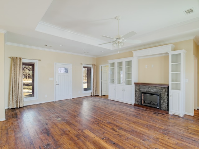 unfurnished living room with ceiling fan, a stone fireplace, ornamental molding, and dark wood-type flooring