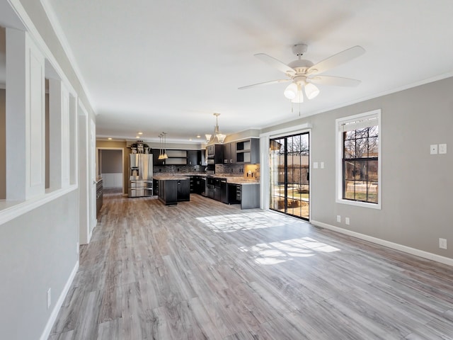 unfurnished living room with ceiling fan with notable chandelier, crown molding, and light hardwood / wood-style flooring