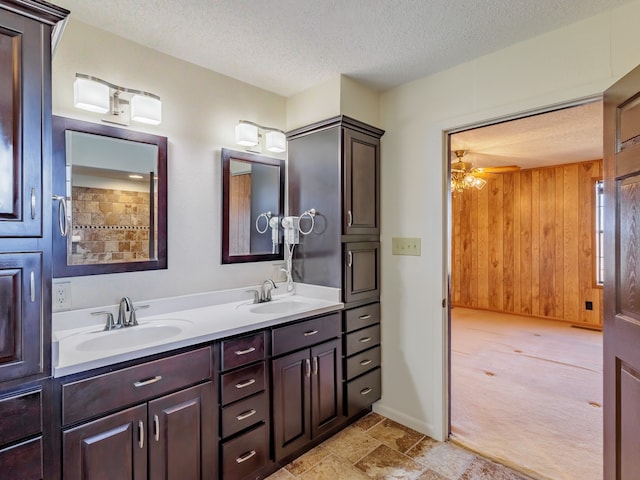 bathroom featuring ceiling fan, vanity, wood walls, and a textured ceiling