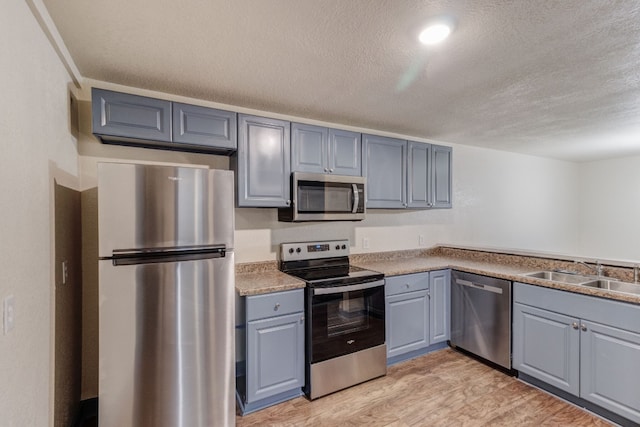 kitchen featuring sink, gray cabinets, appliances with stainless steel finishes, light hardwood / wood-style floors, and a textured ceiling