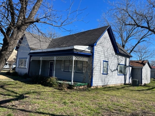 rear view of property with central AC unit and a lawn