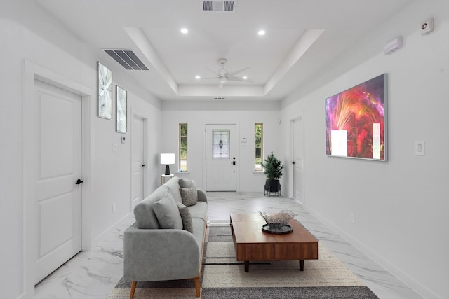 tiled living room with a tray ceiling and ceiling fan