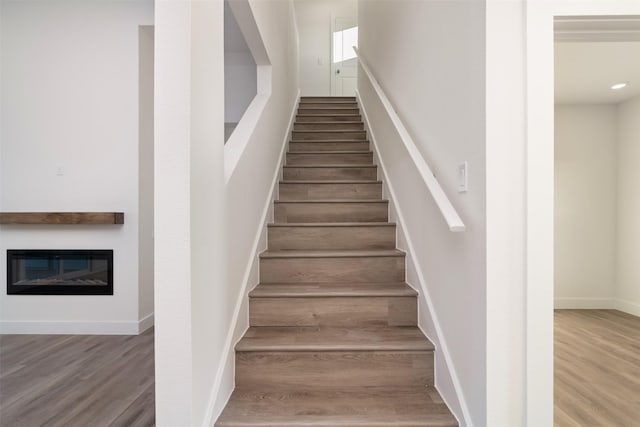 stairs with baseboards, wood finished floors, and a glass covered fireplace