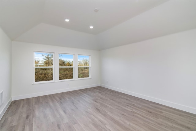 spare room with vaulted ceiling, light wood finished floors, and baseboards