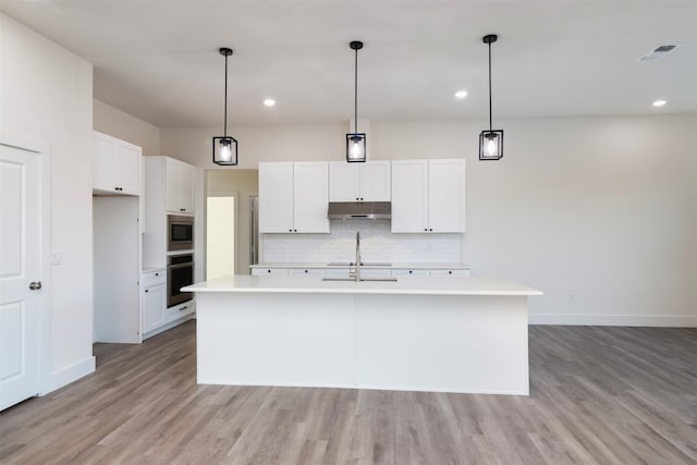 kitchen with under cabinet range hood, stainless steel appliances, visible vents, light countertops, and tasteful backsplash