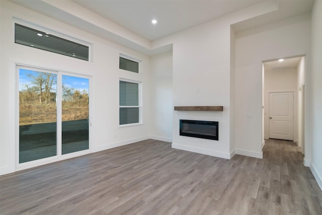 unfurnished living room with a glass covered fireplace, recessed lighting, baseboards, and wood finished floors