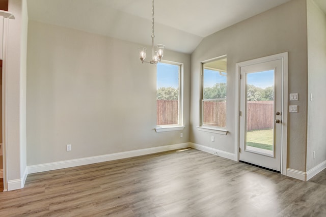 unfurnished dining area with lofted ceiling, hardwood / wood-style floors, and an inviting chandelier