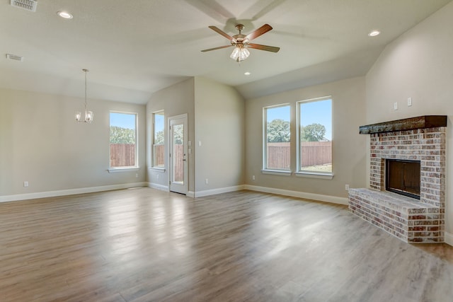 unfurnished living room with ceiling fan with notable chandelier, lofted ceiling, a fireplace, and light hardwood / wood-style flooring