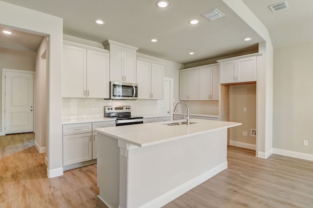 kitchen with an island with sink, sink, light hardwood / wood-style flooring, white cabinetry, and stainless steel appliances