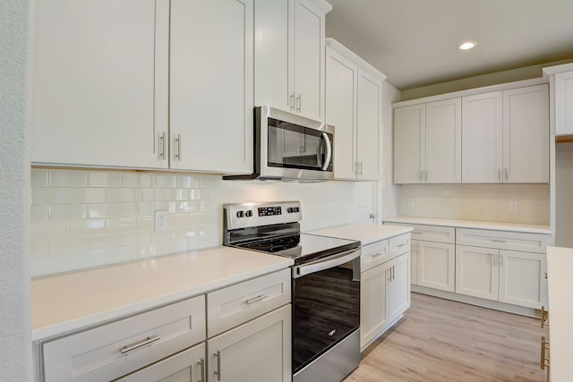 kitchen featuring white cabinets, stainless steel appliances, light hardwood / wood-style floors, and decorative backsplash