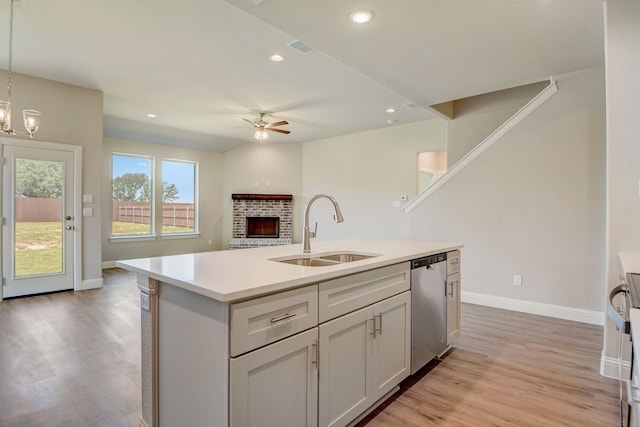 kitchen with sink, decorative light fixtures, a kitchen island with sink, dishwasher, and light hardwood / wood-style floors