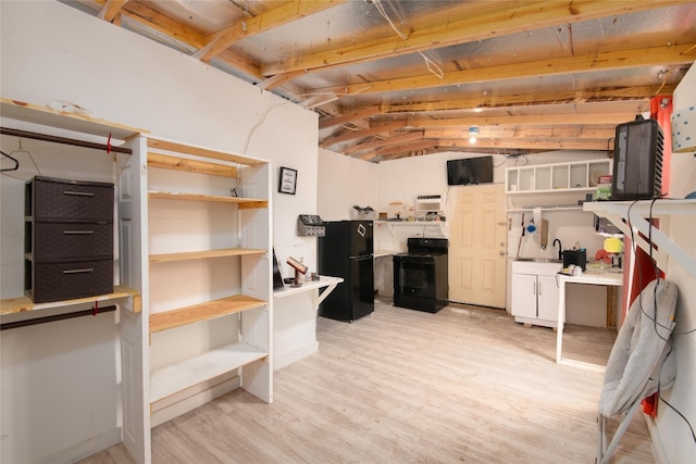 basement with black refrigerator, sink, and light hardwood / wood-style flooring