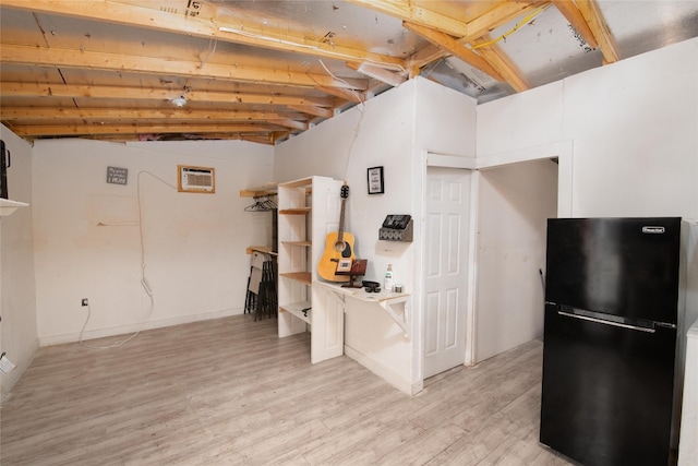 basement featuring a wall mounted AC, light hardwood / wood-style flooring, and black fridge