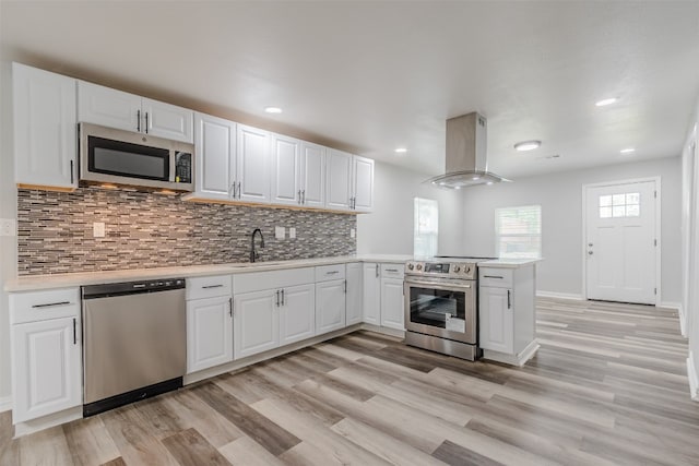 kitchen featuring island range hood, light hardwood / wood-style floors, stainless steel appliances, and kitchen peninsula