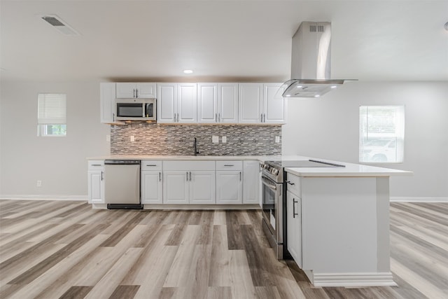 kitchen featuring white cabinetry, light wood-type flooring, stainless steel appliances, island range hood, and tasteful backsplash