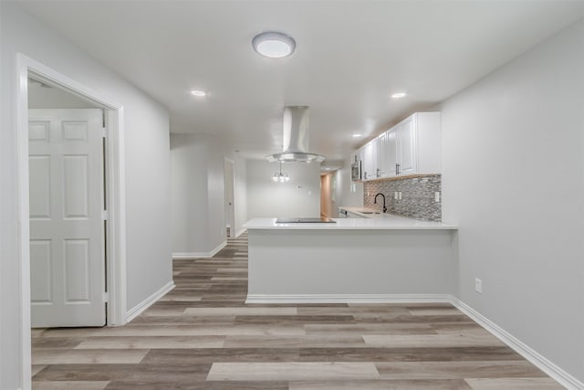 kitchen with backsplash, kitchen peninsula, island exhaust hood, light hardwood / wood-style flooring, and white cabinets