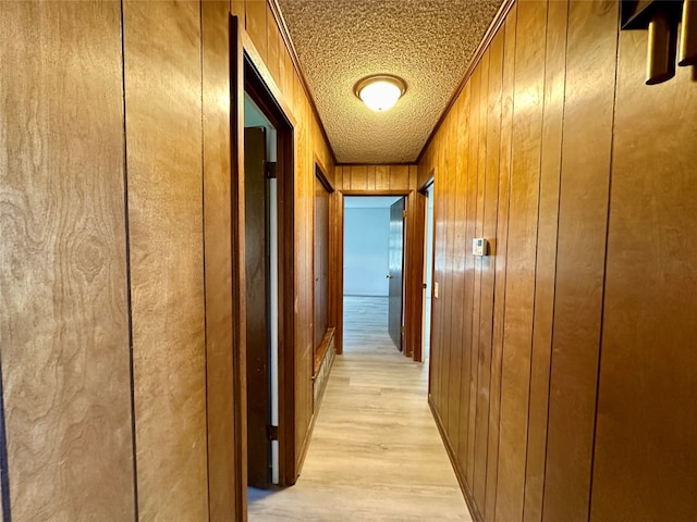 corridor with wooden walls, ornamental molding, light hardwood / wood-style flooring, and a textured ceiling