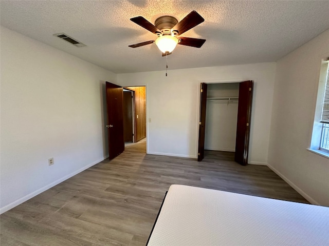 unfurnished bedroom with ceiling fan, a textured ceiling, light wood-type flooring, and a closet