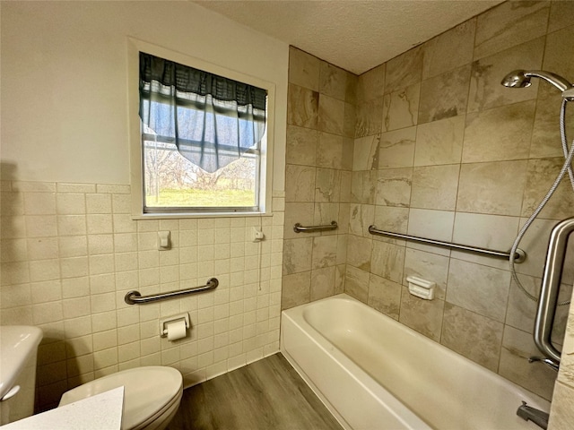 bathroom with tile walls, tiled shower / bath, a textured ceiling, toilet, and hardwood / wood-style flooring