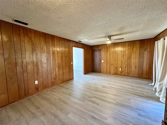 unfurnished room featuring a textured ceiling, wood walls, and light hardwood / wood-style flooring