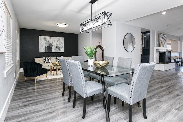 dining area featuring wood-type flooring, a brick fireplace, and an inviting chandelier