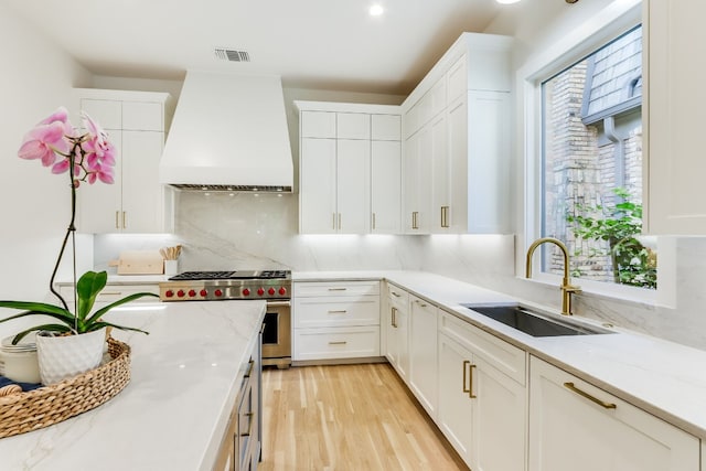 kitchen featuring premium range hood, sink, white cabinetry, tasteful backsplash, and stainless steel stove