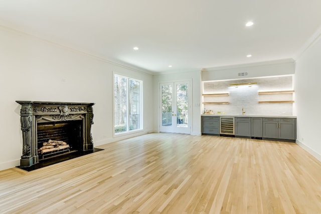 unfurnished living room featuring wine cooler, ornamental molding, a high end fireplace, and light hardwood / wood-style floors