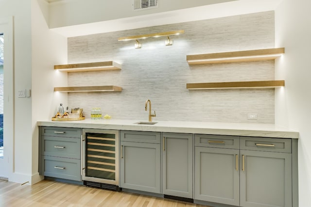 bar featuring wine cooler, light wood-type flooring, sink, and backsplash