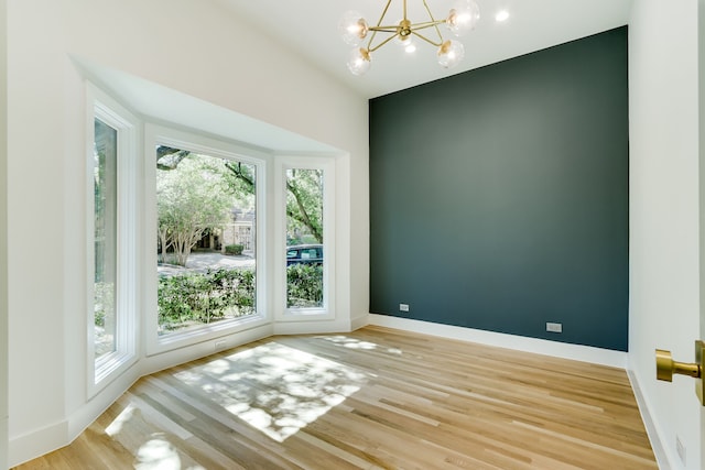 unfurnished room featuring a notable chandelier and light wood-type flooring