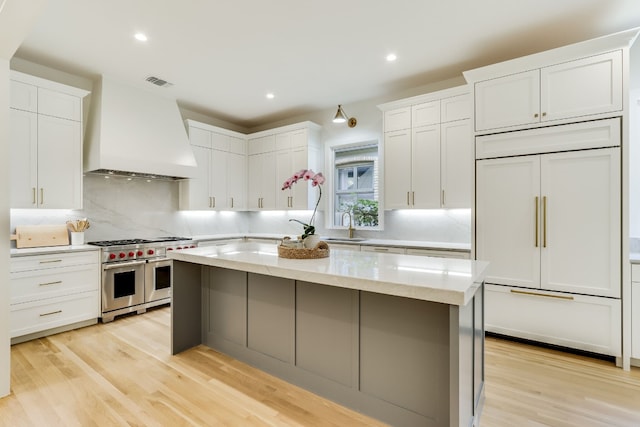 kitchen with high quality appliances, premium range hood, a center island, and white cabinets