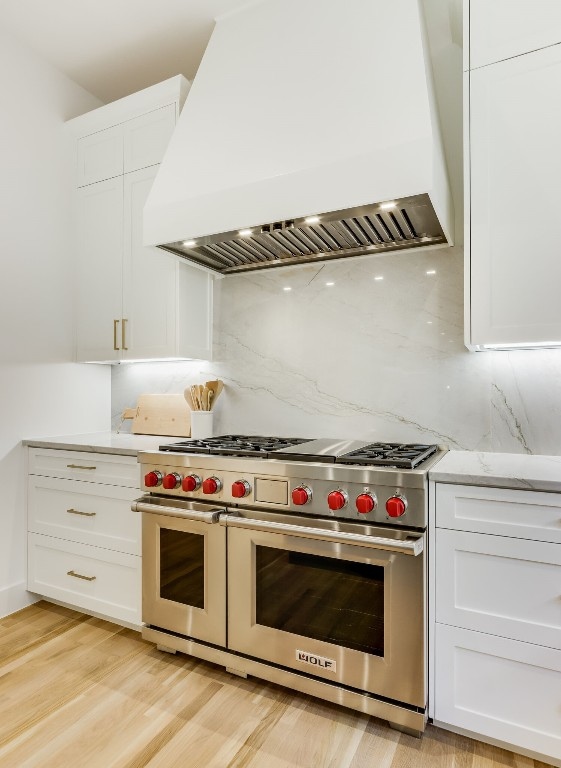 kitchen with tasteful backsplash, premium range hood, white cabinets, and range with two ovens