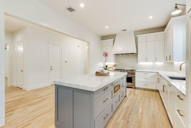 kitchen with appliances with stainless steel finishes, white cabinetry, sink, a center island, and custom range hood